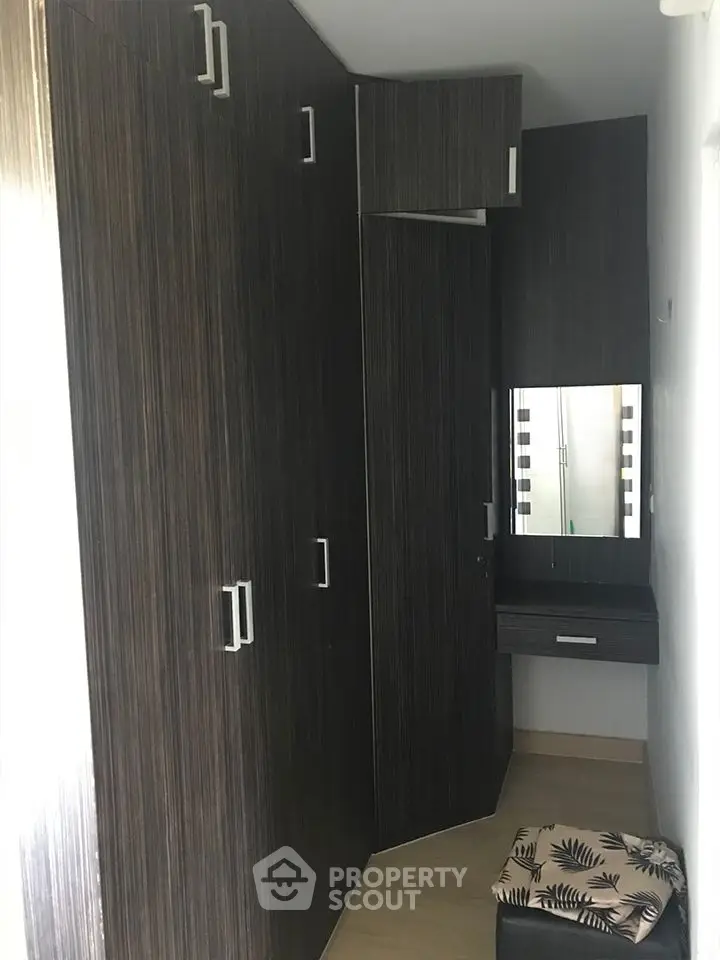 Modern walk-in closet with sleek dark wood cabinetry and built-in vanity mirror.