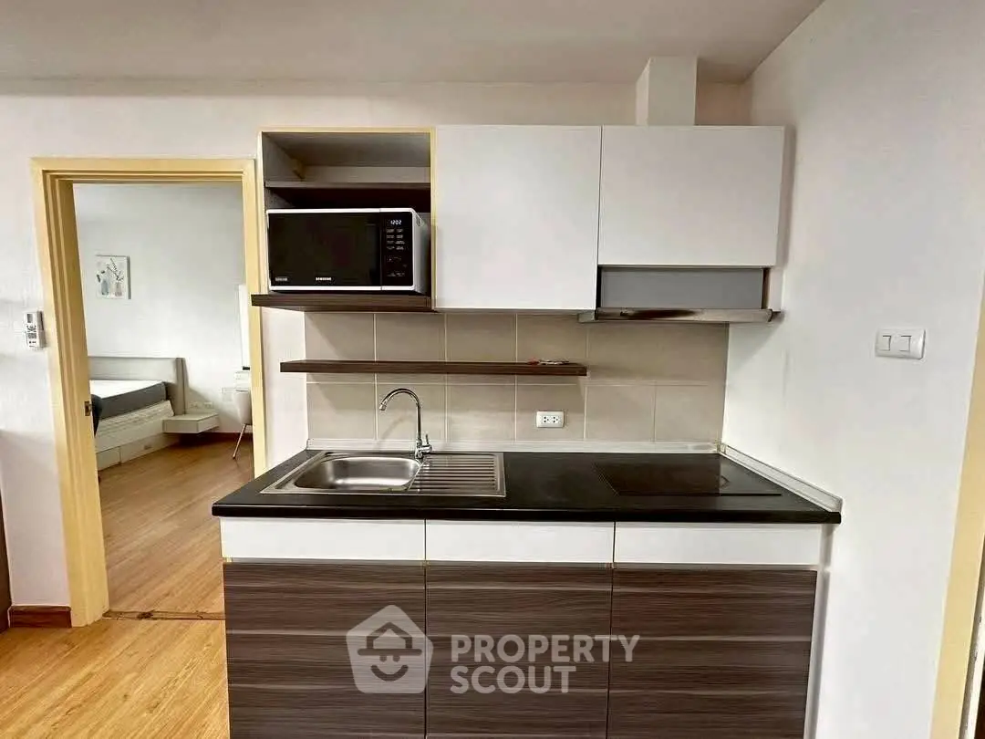 Modern compact kitchen with sleek cabinetry and built-in microwave in a cozy apartment.