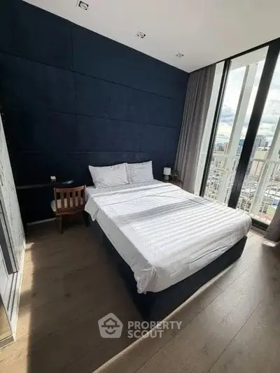 Modern bedroom with large windows and city view, featuring stylish decor and cozy ambiance.