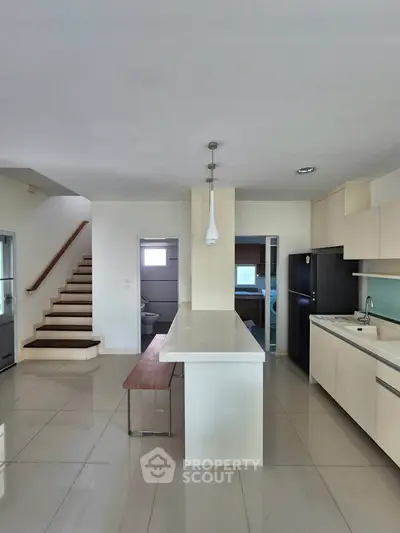 Modern kitchen with sleek white cabinetry and island, featuring open layout and staircase view.