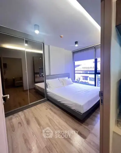 Modern bedroom with mirrored closet and large window offering natural light.