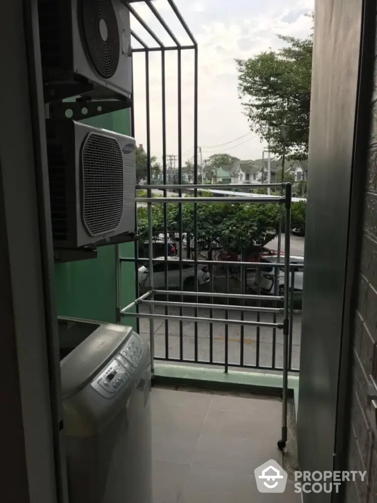 Compact balcony with washing machine and air conditioning unit overlooking street view.