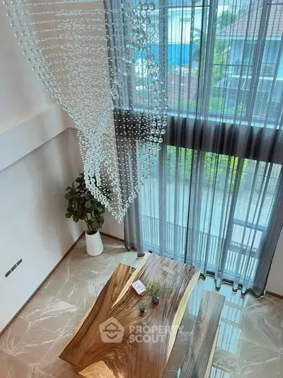Luxurious modern living room with elegant chandelier and wooden table, featuring floor-to-ceiling windows.