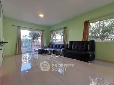 Spacious living room with black leather sofas and large windows offering garden views.
