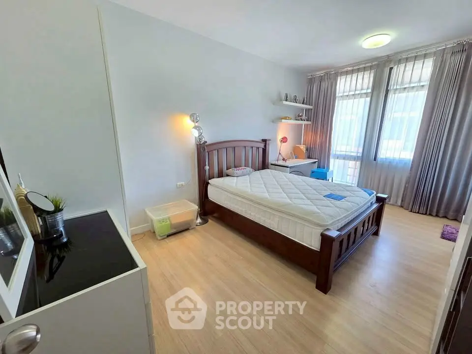 Spacious bedroom with wooden bed frame and natural light through large windows.