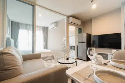 Modern open-plan living room with kitchen and bedroom, featuring sleek furniture and natural light.