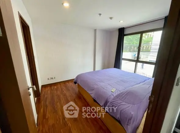 Cozy bedroom with wooden flooring and large window offering natural light