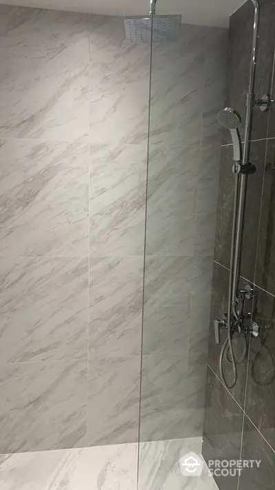 Sleek modern bathroom with marble tiles and glass shower enclosure, featuring a luxurious rainfall showerhead and handheld sprayer for a spa-like experience.