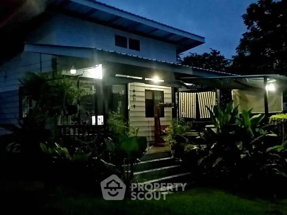 Charming evening view of a cozy home with lush garden and inviting porch lighting.