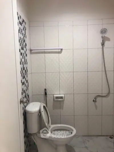 Modern bathroom with tiled walls and showerhead, featuring a sleek toilet design.