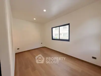 Spacious empty room with wooden flooring and large window, perfect for customization.