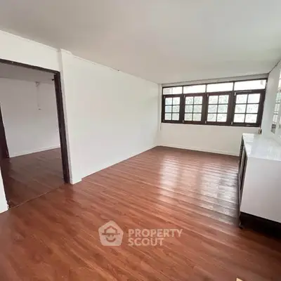 Spacious empty room with wooden flooring and large windows, perfect for customization.