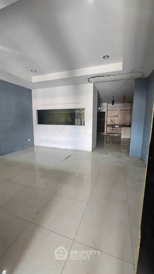 Spacious open-plan living area with modern tiled flooring and adjacent kitchen space.