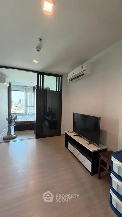 Modern living room with TV and air conditioning, leading to a bedroom with city view.