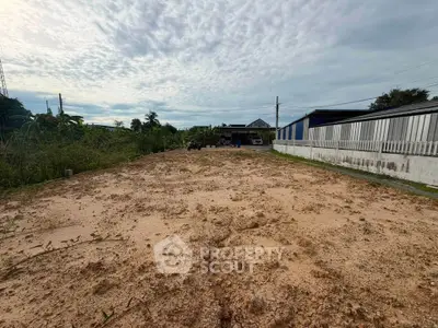 Expansive vacant land plot with potential for development, surrounded by greenery and nearby structures.