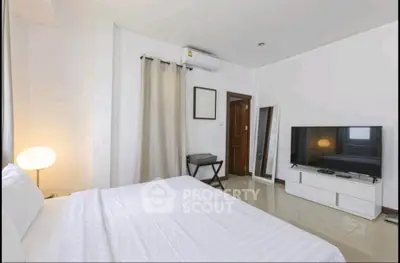 Spacious bedroom with modern decor and large TV, perfect for relaxation.