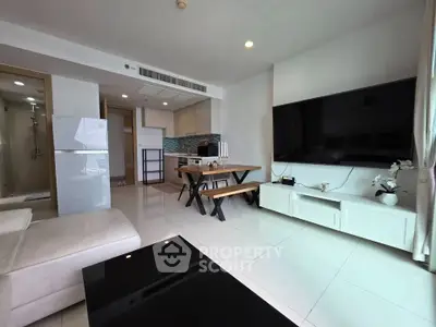 Modern living room with sleek furniture and large TV, open layout with kitchen area, bright and spacious.