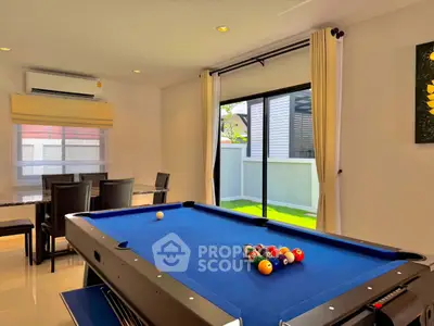 Stylish living room with pool table and dining area, featuring large windows and modern decor.