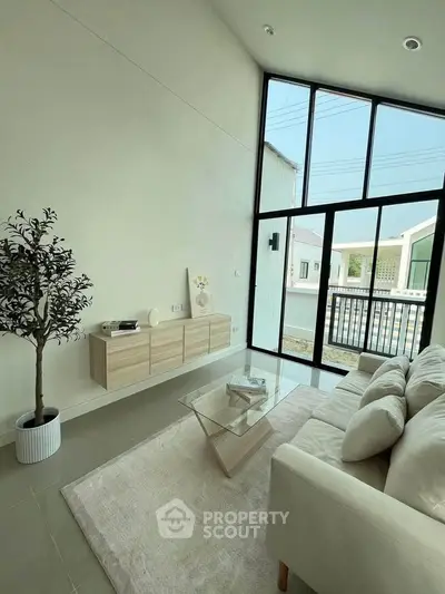 Modern living room with high ceilings and large windows, featuring a cozy sofa and minimalist decor.