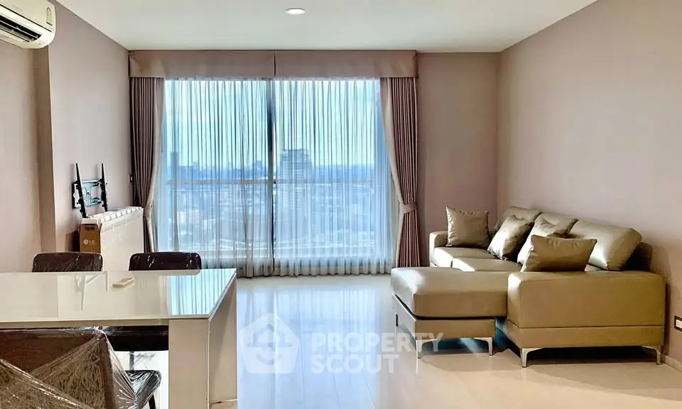 Spacious modern living room with large windows and city view, featuring elegant furniture and natural light.