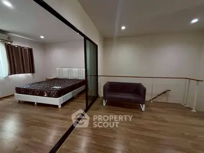 Spacious bedroom with modern decor and large mirror sliding doors, featuring wooden flooring and cozy seating area.