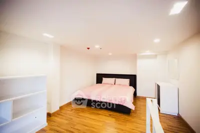 Spacious bedroom with wooden flooring and modern furnishings in a cozy apartment.