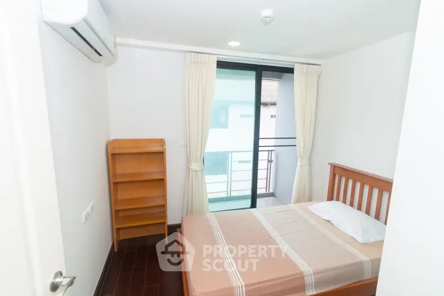 Cozy bedroom with balcony access, featuring a wooden bed frame and air conditioning, ideal for comfort seekers.