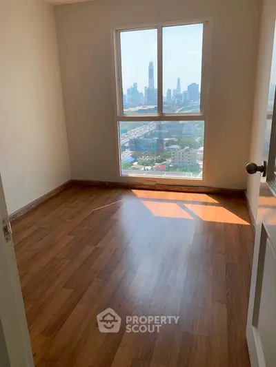 Bright empty room with large window offering stunning city view and wooden flooring.