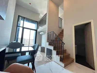 Modern duplex apartment with high ceilings and stylish staircase, featuring a spacious living area and large windows.