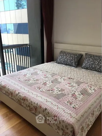 Cozy bedroom with floral bedding and large window offering natural light and city view.
