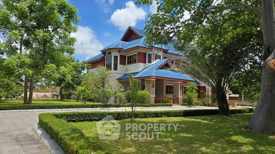 Charming two-story house with blue roof surrounded by lush greenery and manicured lawn.
