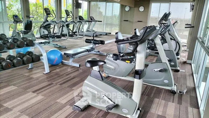 Spacious gym with modern exercise equipment and large windows offering natural light.