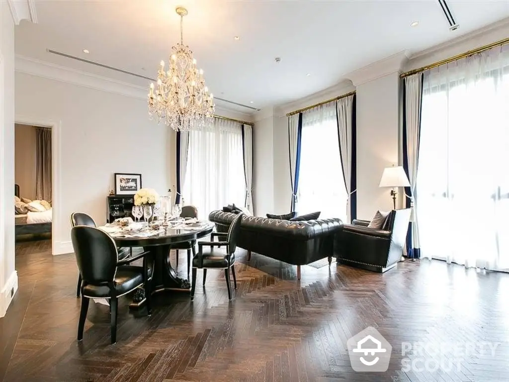 Luxurious open-plan living space with elegant chandelier, rich hardwood floors, and sophisticated dark leather furniture.