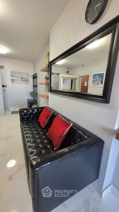 Stylish living room with black leather sofa and red cushions, large wall mirror, and modern decor.