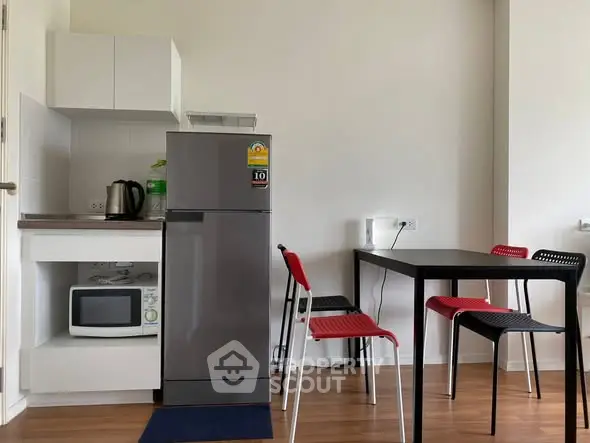 Modern compact kitchen with dining area, featuring a fridge, microwave, and stylish chairs.
