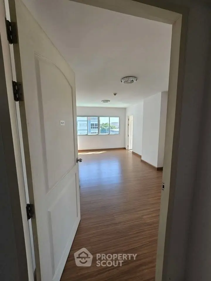 Spacious empty room with wooden flooring and large windows offering natural light.