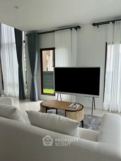 Modern living room with large windows, stylish curtains, and a sleek TV setup.
