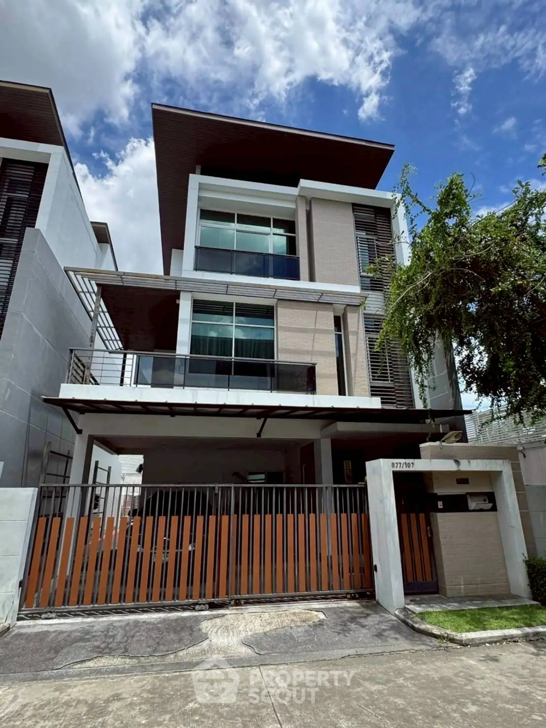 Modern multi-story house with sleek design and gated entrance under a clear blue sky.