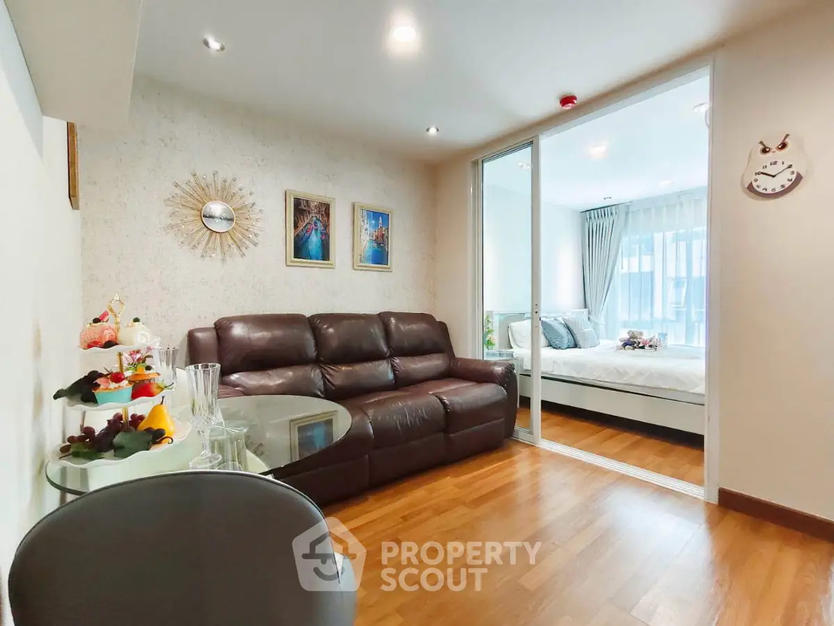 Modern living room with glass partition leading to a cozy bedroom, featuring stylish decor and wooden flooring.