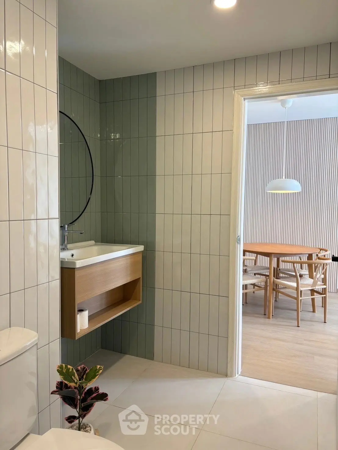 Modern bathroom with sleek tiles and view into dining area, showcasing contemporary design.