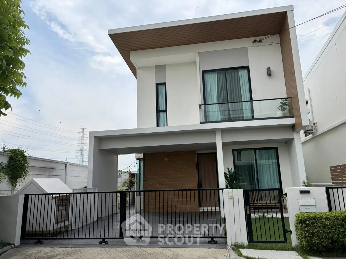 Modern two-story house with sleek design and gated entrance, featuring large windows and a minimalist facade.