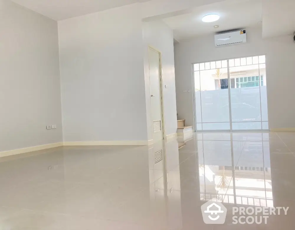 Spacious and bright living room with glossy tiled flooring, large windows allowing ample natural light, and a modern air conditioning unit, perfect for comfortable urban living.