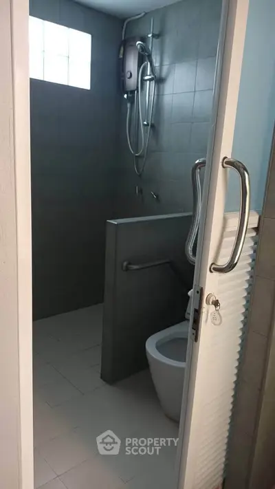 Modern bathroom with shower and toilet, featuring sleek gray tiles and a window for natural light.