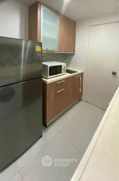 Modern compact kitchen with stainless steel fridge and microwave in sleek apartment.