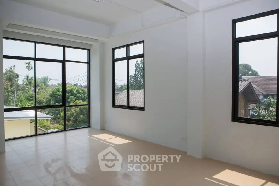 Spacious room with large windows offering a serene garden view, perfect for a bright and airy living space.