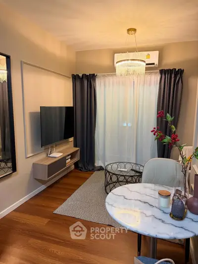 Modern living room with elegant decor, featuring a wall-mounted TV, stylish chandelier, and cozy seating area.