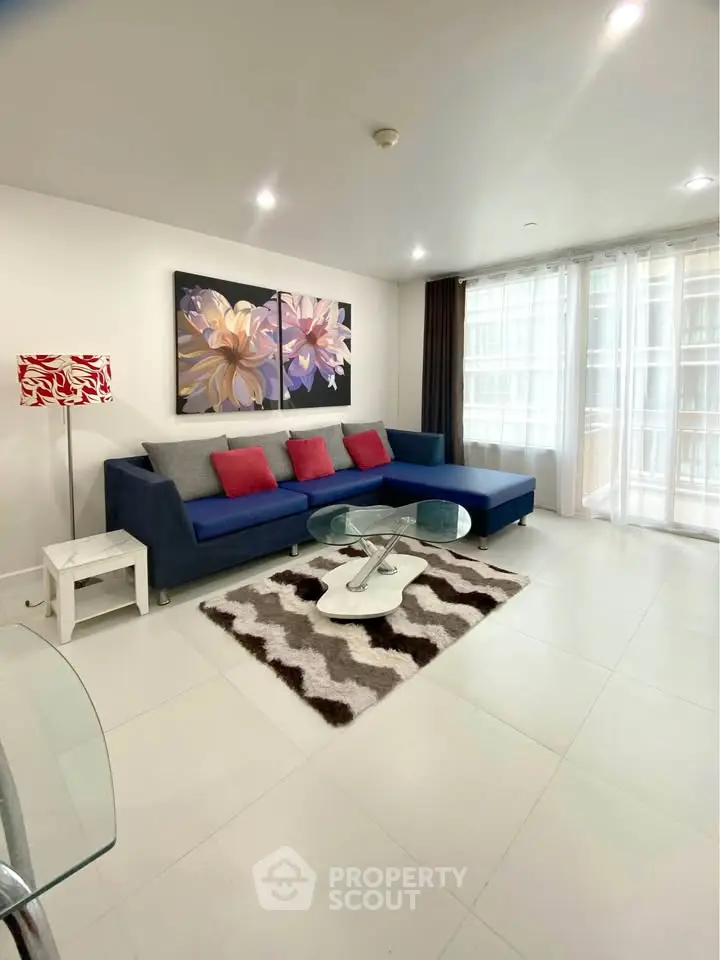 Modern living room with stylish decor, featuring a large blue sofa, abstract art, and natural light from large windows.