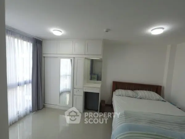 Bright bedroom with large window and built-in wardrobe in modern apartment.