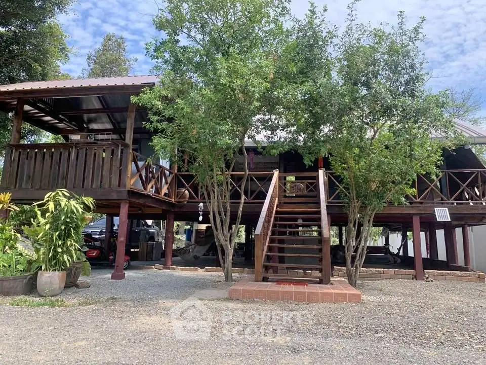 Charming elevated wooden house with lush greenery and spacious outdoor deck, perfect for serene living.