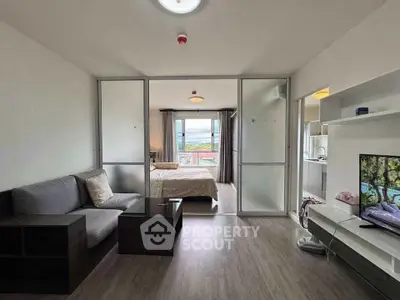 Modern open-plan living room with bedroom view, featuring sleek furniture and natural light.
